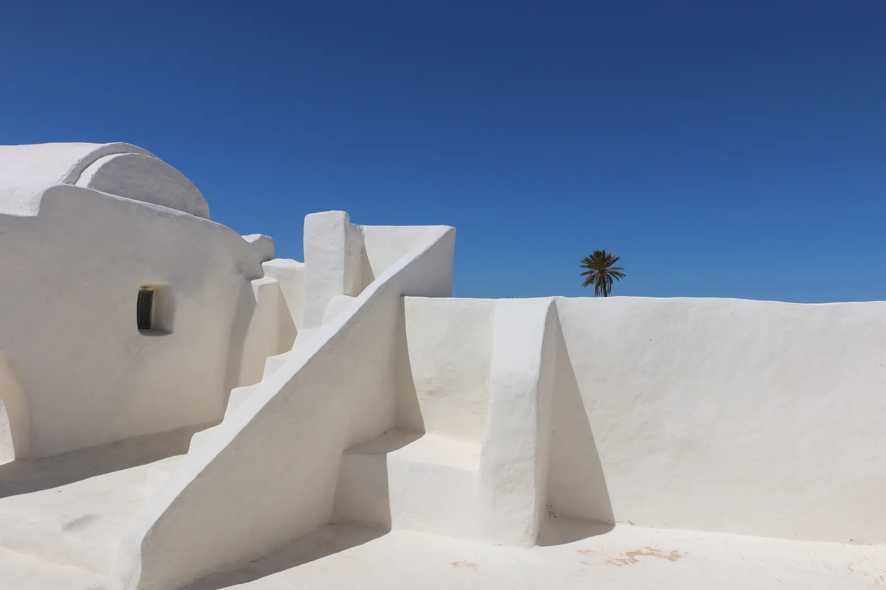 Mosquée blanchie à la chaux sous un ciel bleu, un palmier au loin, à Djerba