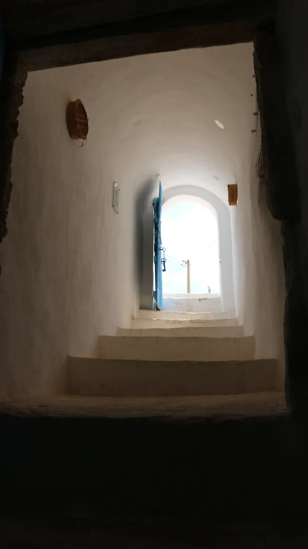 Escalier blanchi à la chaux montant vers une porte bleue ouverte sur le ciel