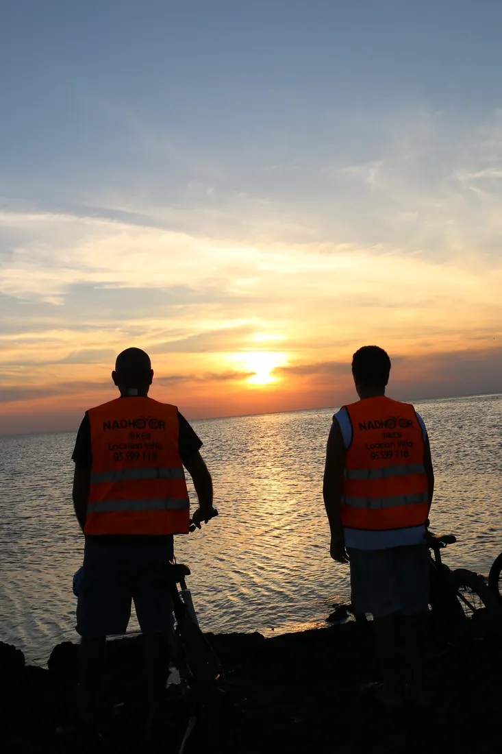 Un père et son fils face au soleil couchant, leurs vélos à côté