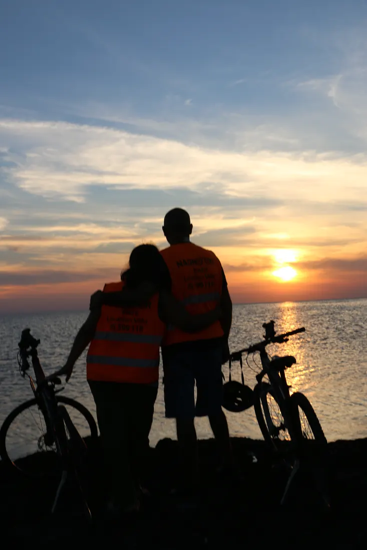 Un couple enlacé face au coucher du soleil, entre deux vélos